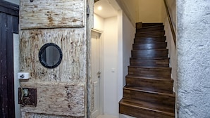 A rustic wooden door with a round mirror and a mailbox, leading to a wooden staircase with a textured wall on the right. - Luna Rooms and Studios (Rovinj)