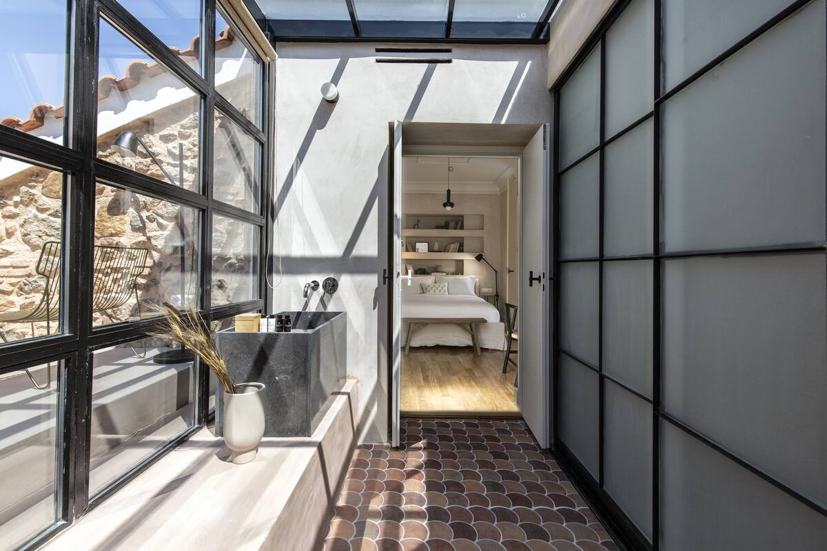 A modern interior with a glass wall leading to a bedroom, a bathtub, and a tiled floor.