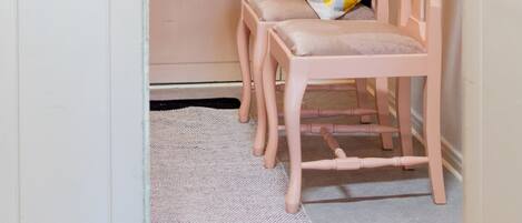A room with a white door marked with numbers, a pink chair with a striped pillow, and a textured wall art piece.
