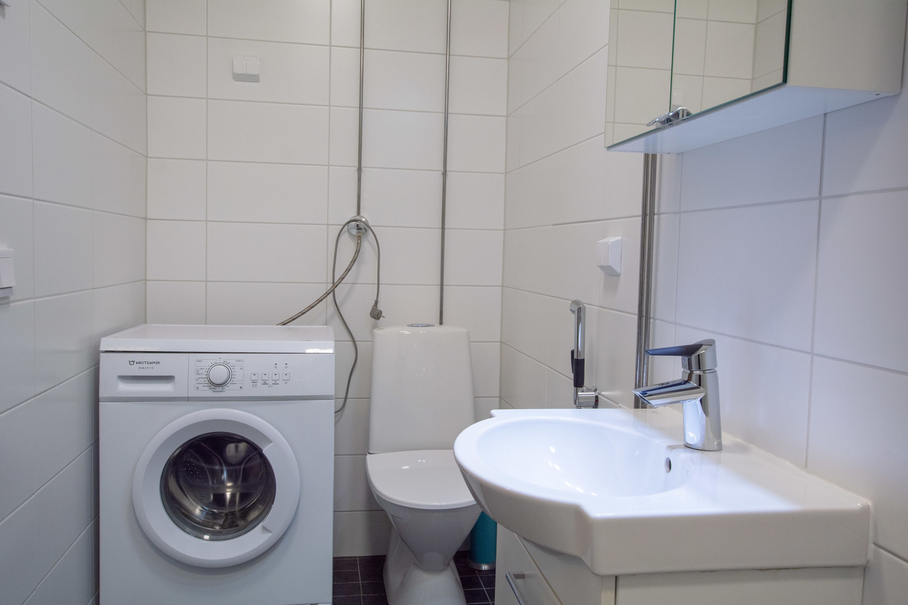 Um banheiro moderno com máquina de lavar, vaso sanitário e pia.