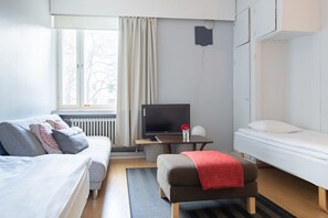 A modern hotel room with a sofa, a small table with a TV, a bed, and a window with curtains.