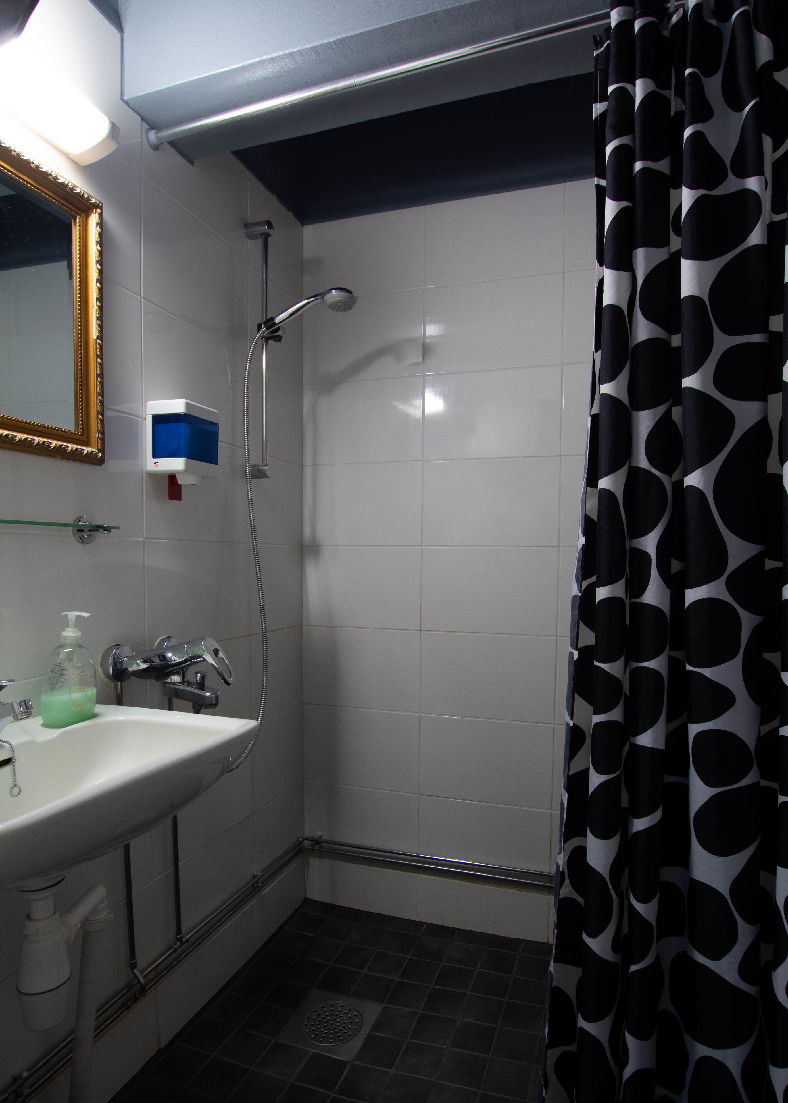 A bathroom with a white sink, a mirror, a shower with a black and white polka dot curtain, and a soap dispenser.