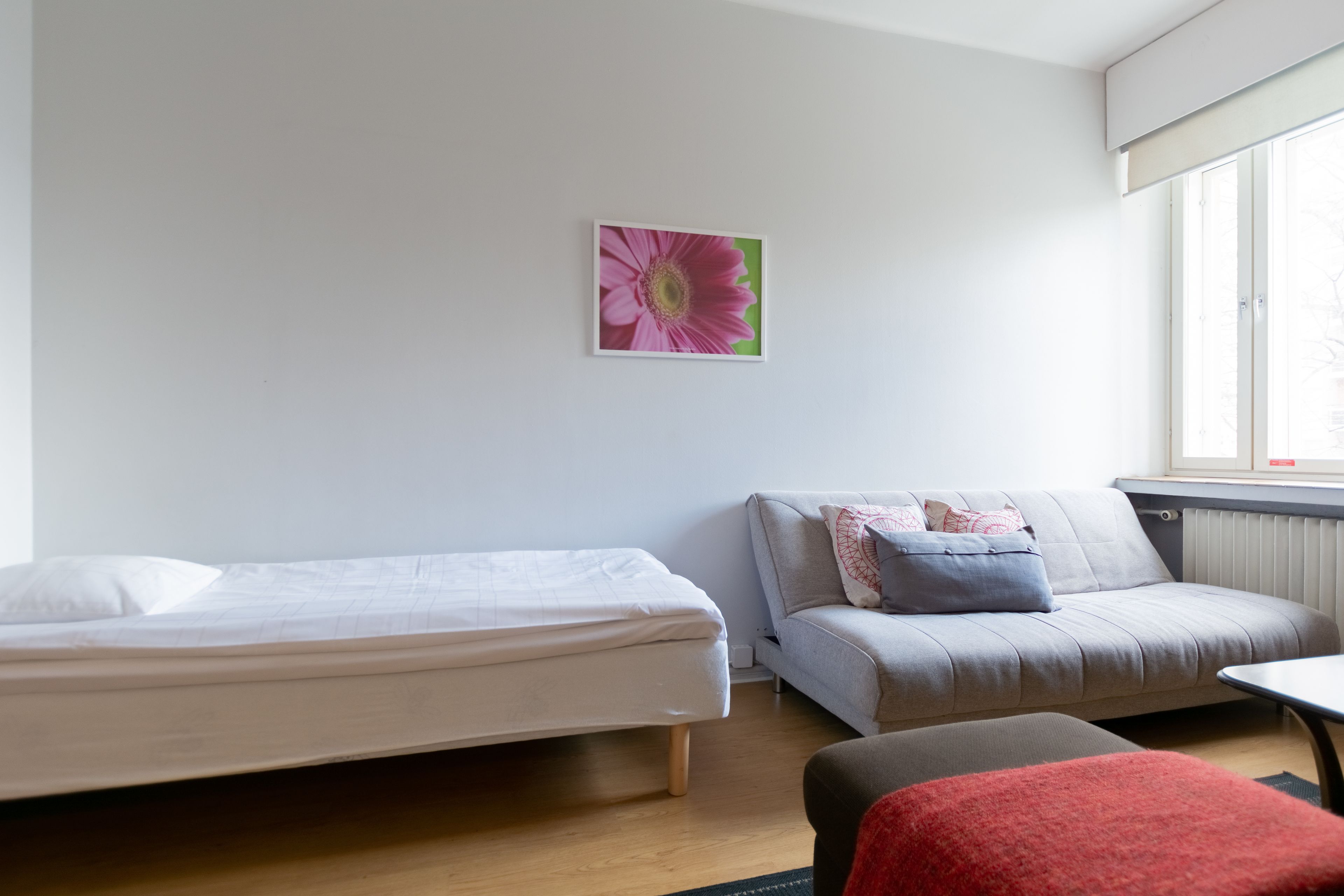 A bedroom with a bed, a sofa, a red chair, and a window with blinds.