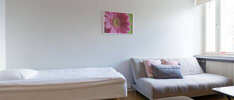 A bedroom with a bed, a sofa, a red chair, and a window with blinds.