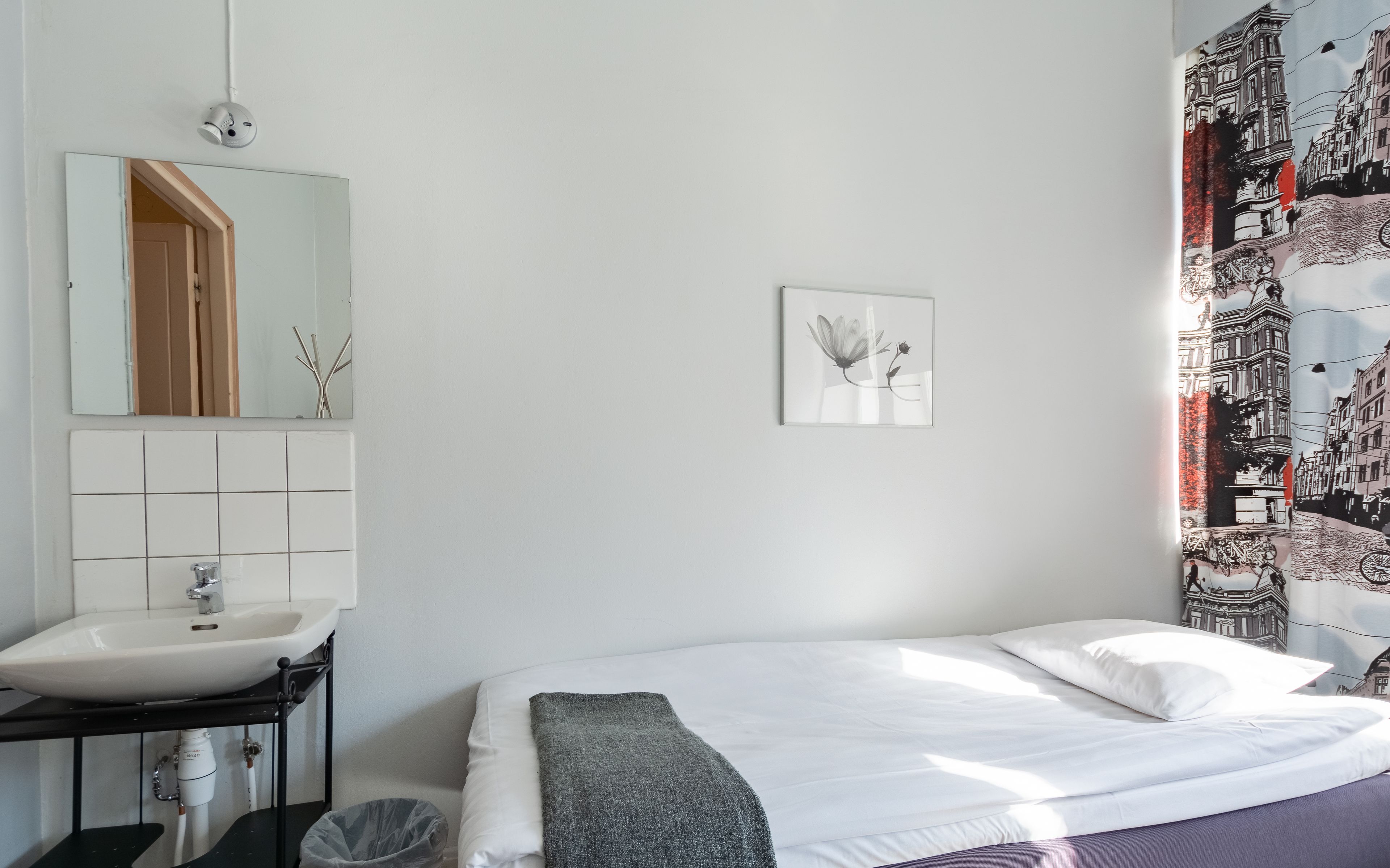 A bedroom with a white bed, a bathroom with a sink and mirror, and a wall with a framed picture.
