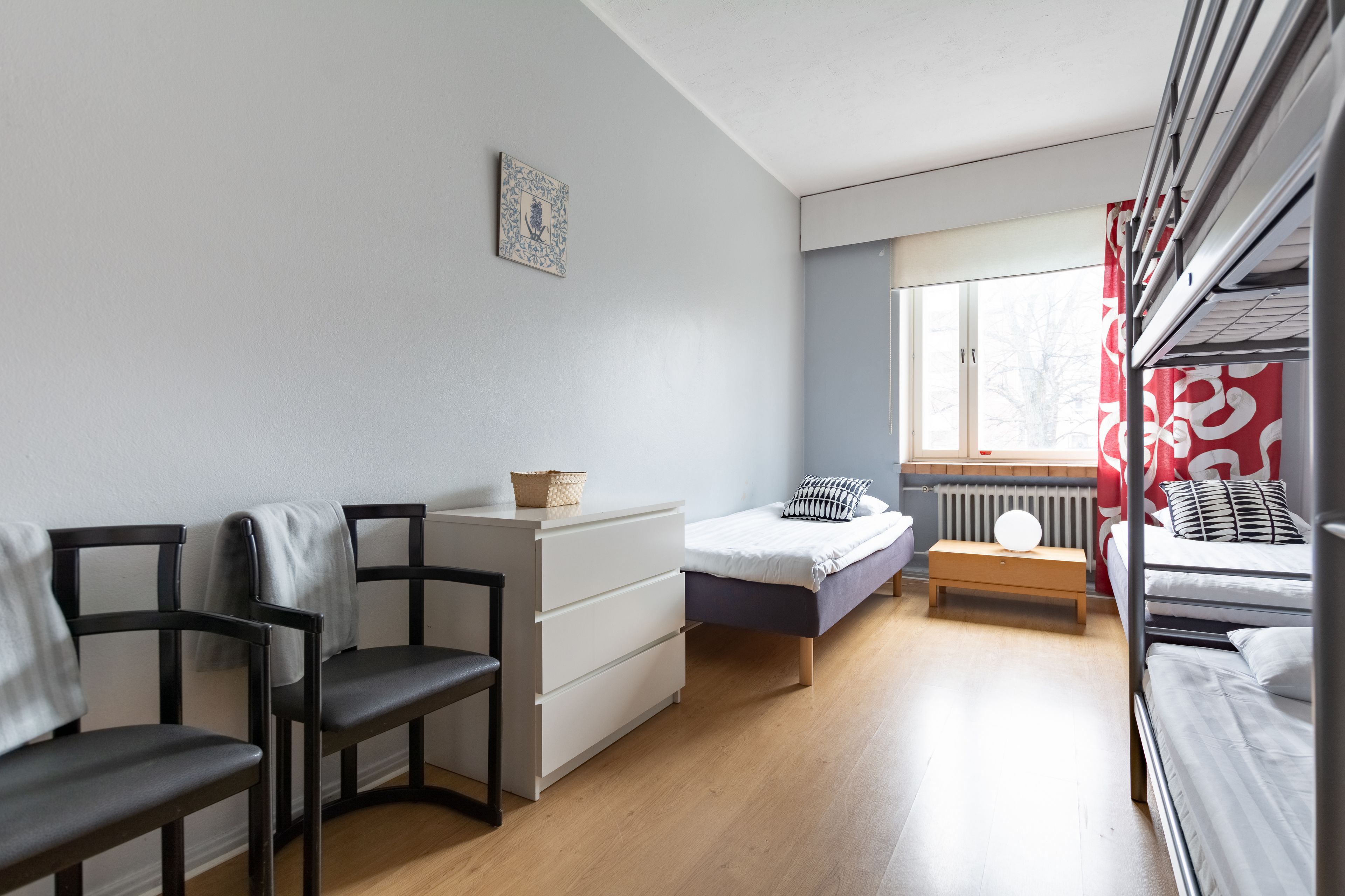 Une petite pièce comprenant un lit, un bureau, deux chaises et une fenêtre.