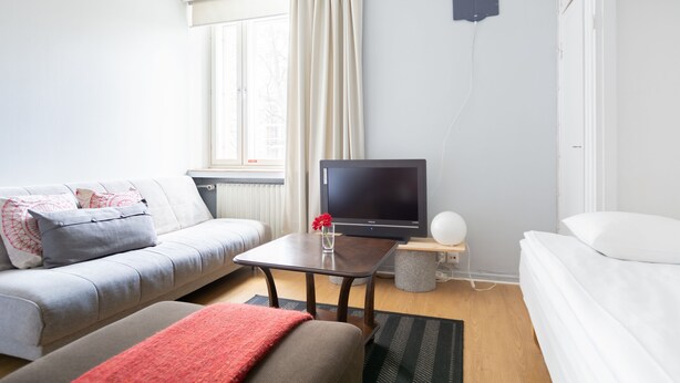 A modern living room with a sofa, a coffee table, a TV, and a bed. - Hostel Buisto (Pori)