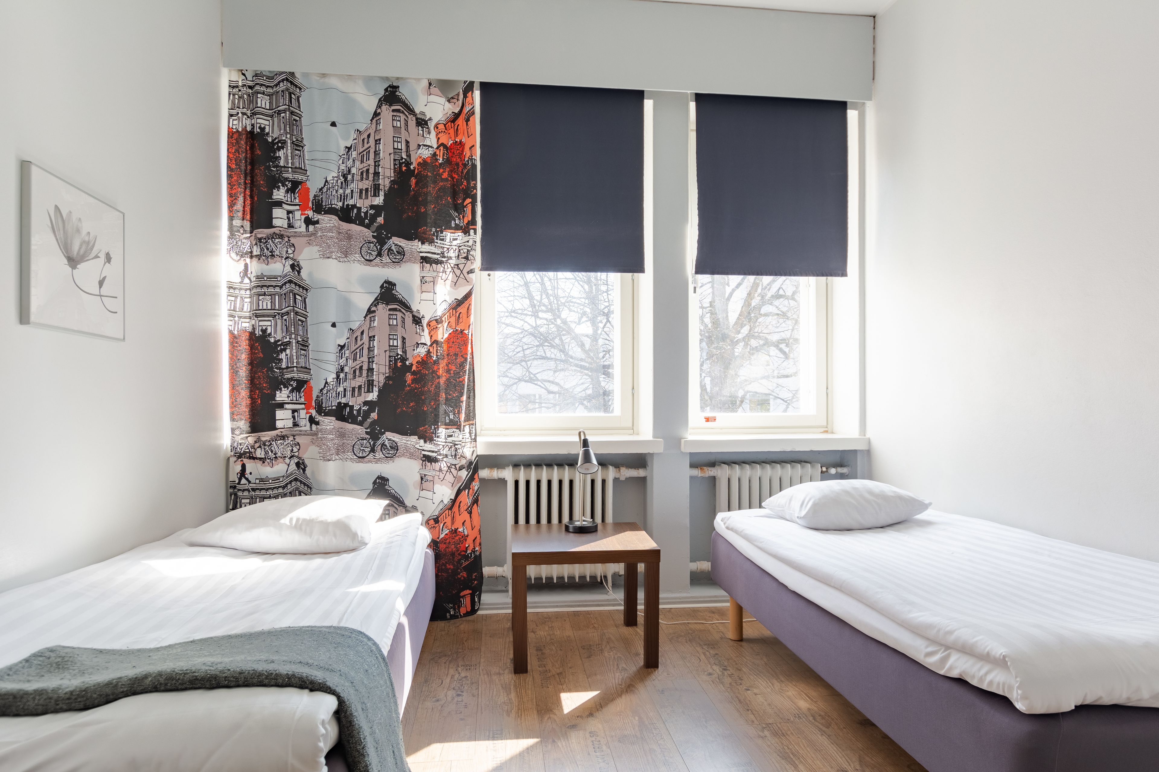 Une chambre avec deux lits, une petite table et un radiateur.