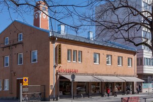 Rakennuksessa on kellotorni, kyltti, jossa lukee ”Palokunta”, ja sen edessä on kaupan edusta, jossa on markiisi.