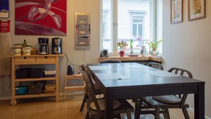 A dining area with a wooden table and chairs, a coffee station, and a window with a view of buildings. - Hostel Buisto (Pori)