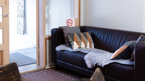A dark leather sofa with patterned cushions, a fur throw, and a 'no smoking' sign on the wall. - Hostel Buisto (Pori)