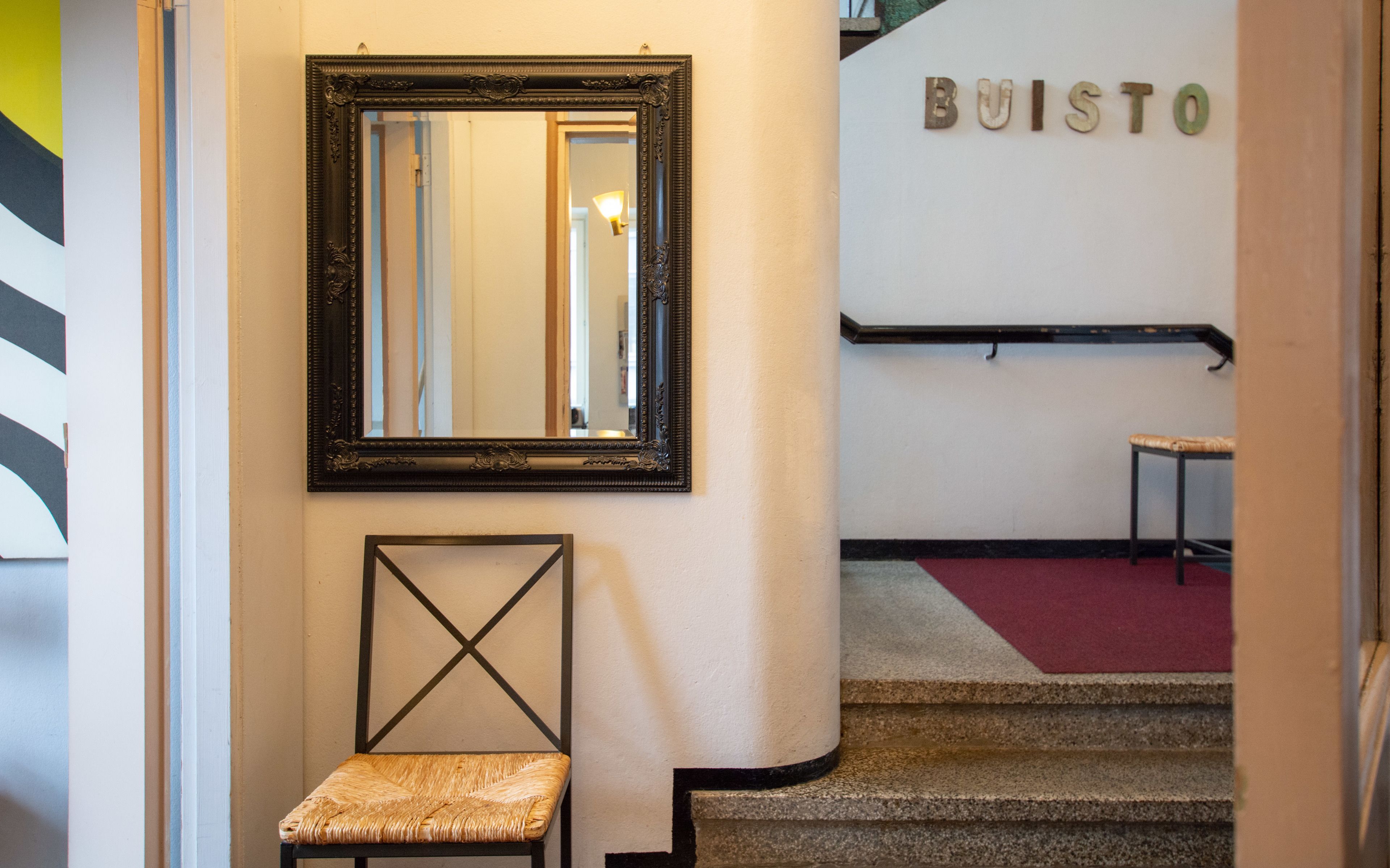A hallway with a mirror, a chair, and a staircase leading to a room labeled "BUISTO".