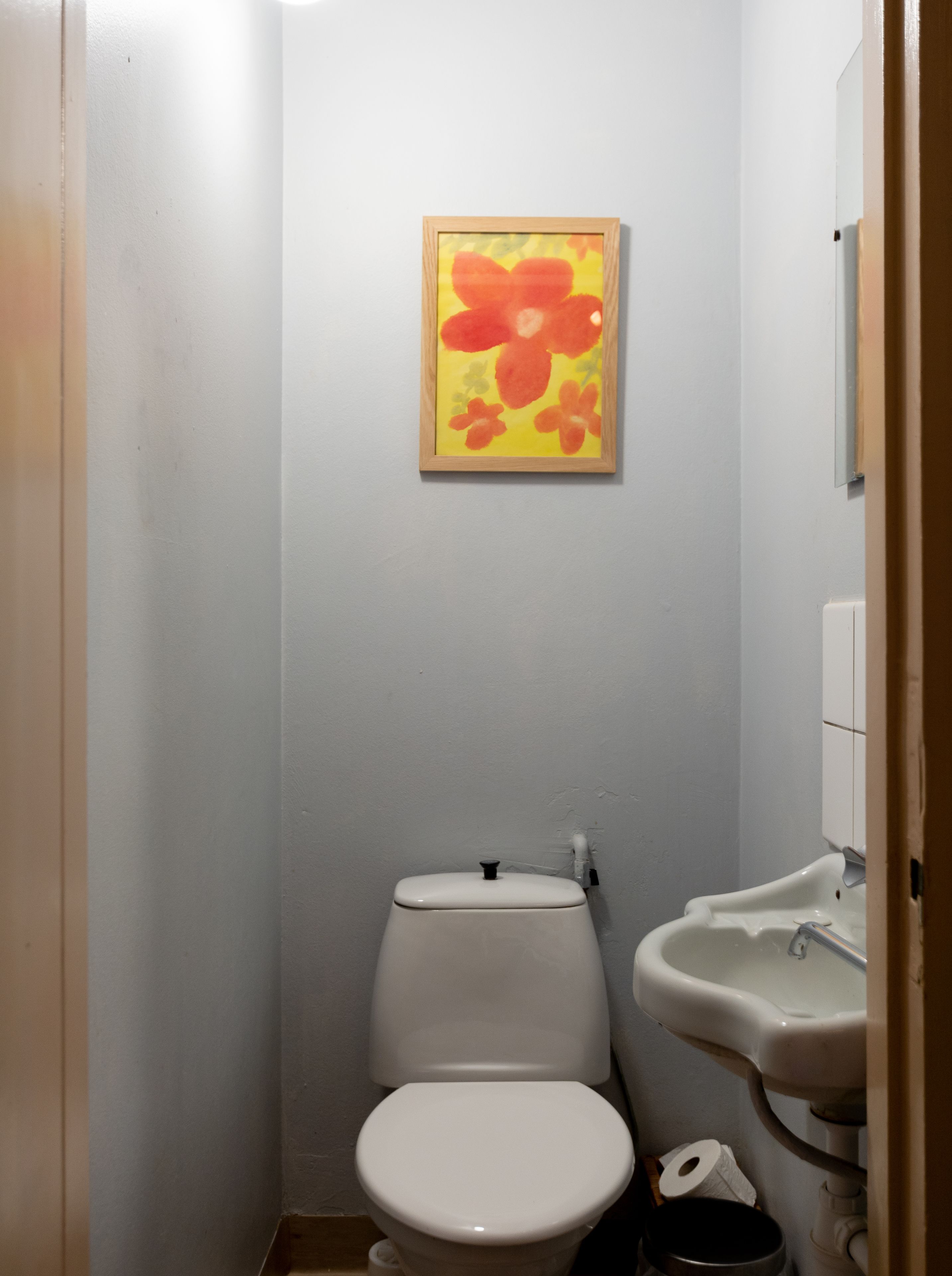 Ein kleines Badezimmer mit Toilette, Waschbecken und einem gerahmten Blumenbild an der Wand.