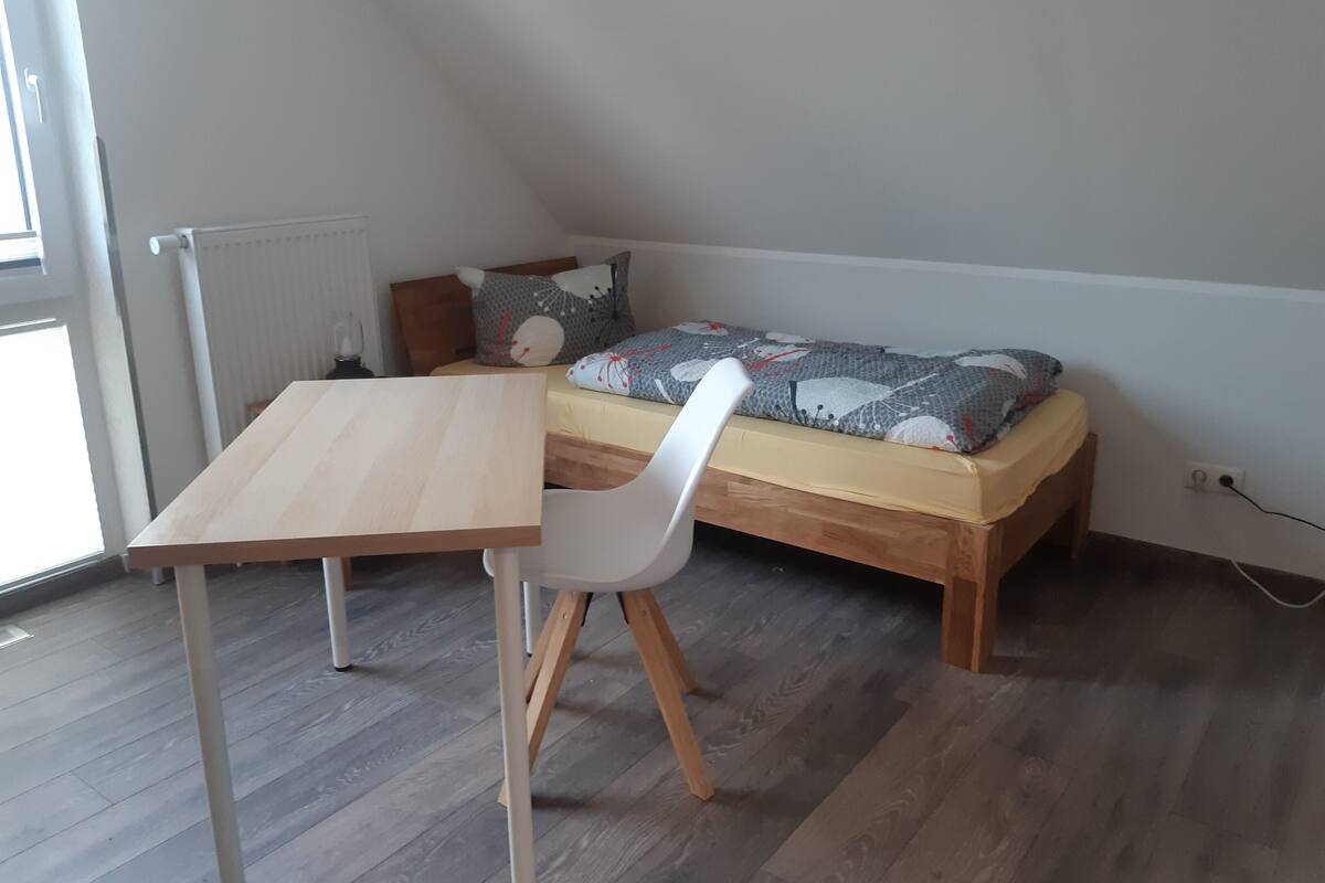 A small room with a wooden bed, a white chair, and a wooden table.