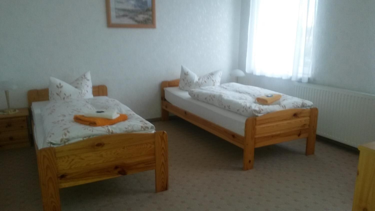 Two wooden beds with floral bedding in a room with a radiator and a window with curtains.