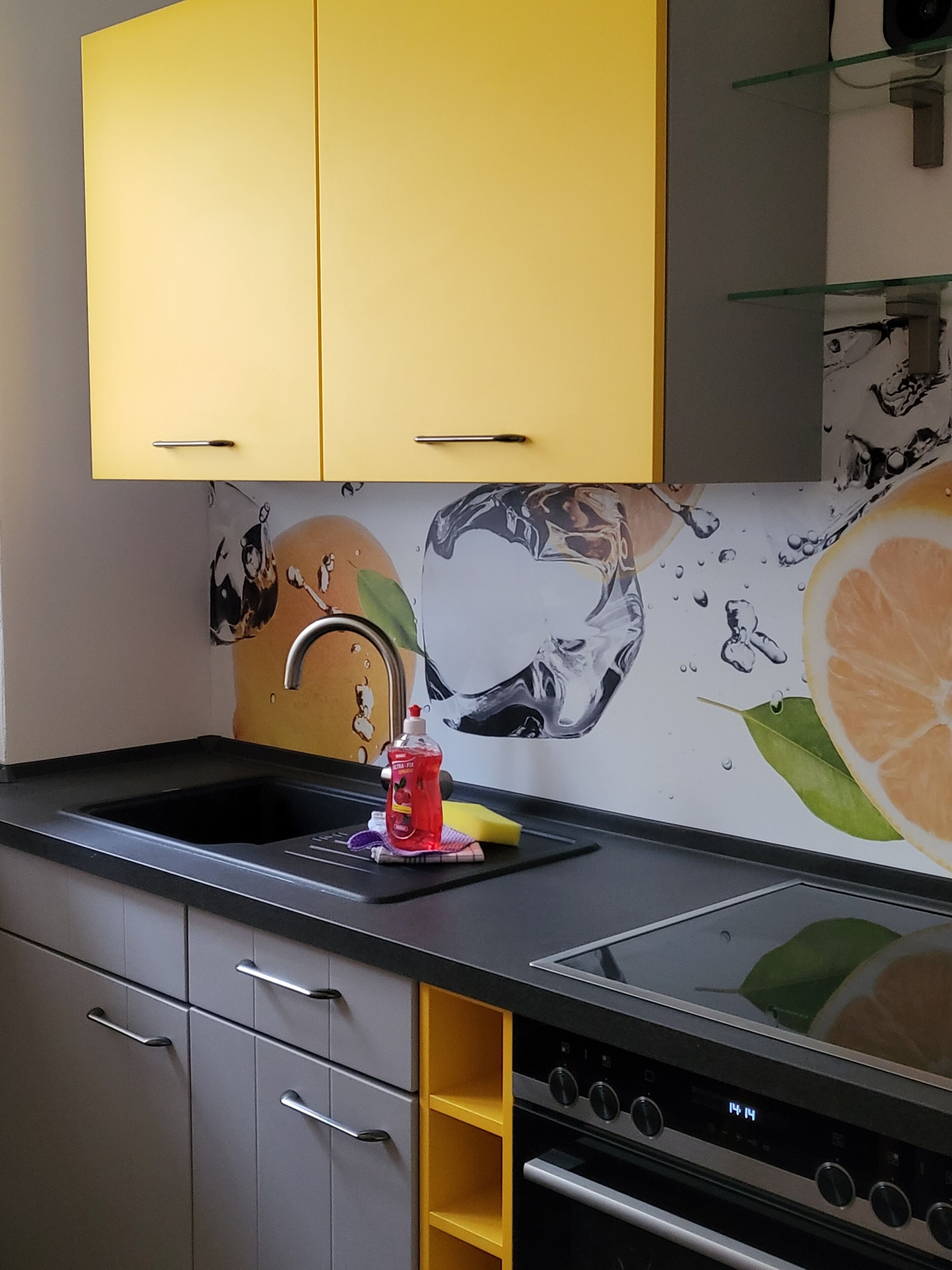 A kitchen with a black countertop, a sink, and a stove. There is a yellow cabinet above the sink and a mural on the wall behind the stove.