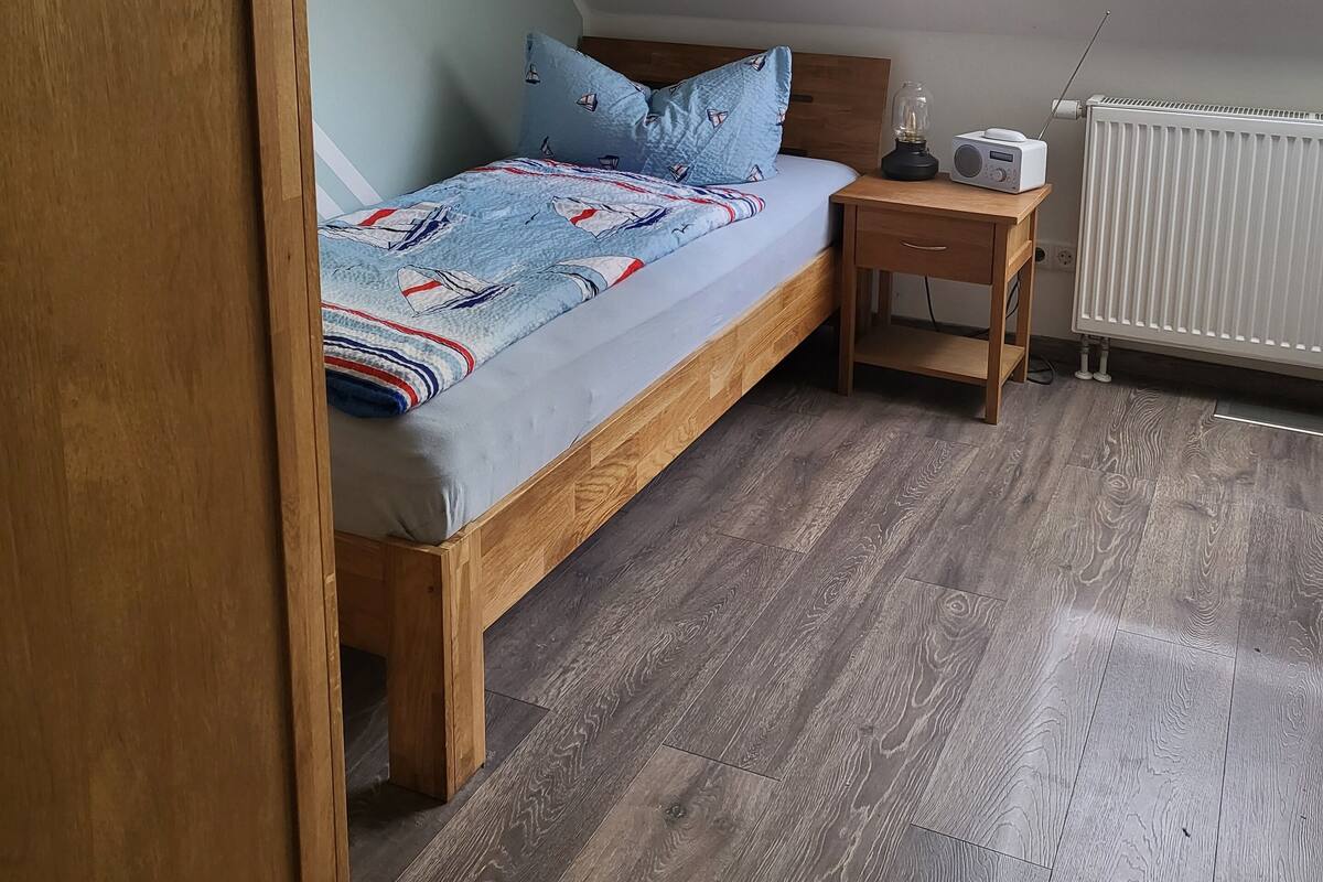 A bedroom with a wooden bed, a bedside table with a radio, and a radiator.