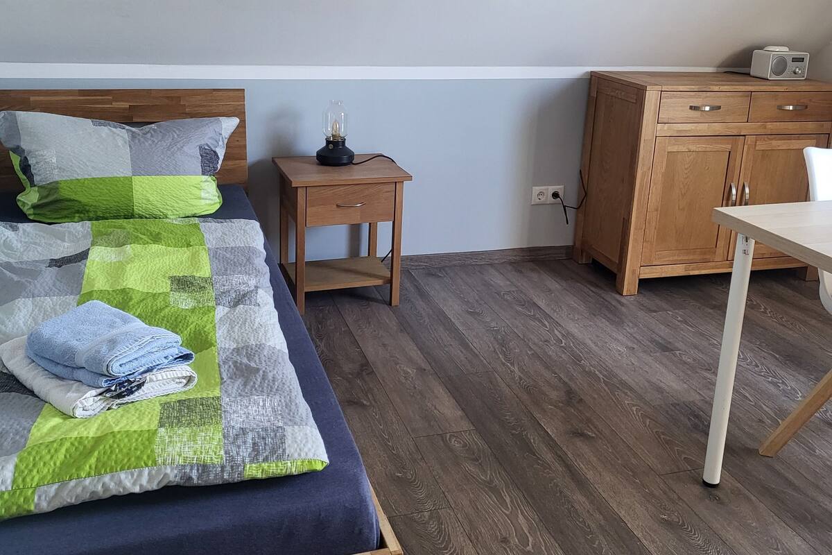 A bedroom with a wooden bed, a bedside table with a lamp, a radio, and a wooden cabinet.