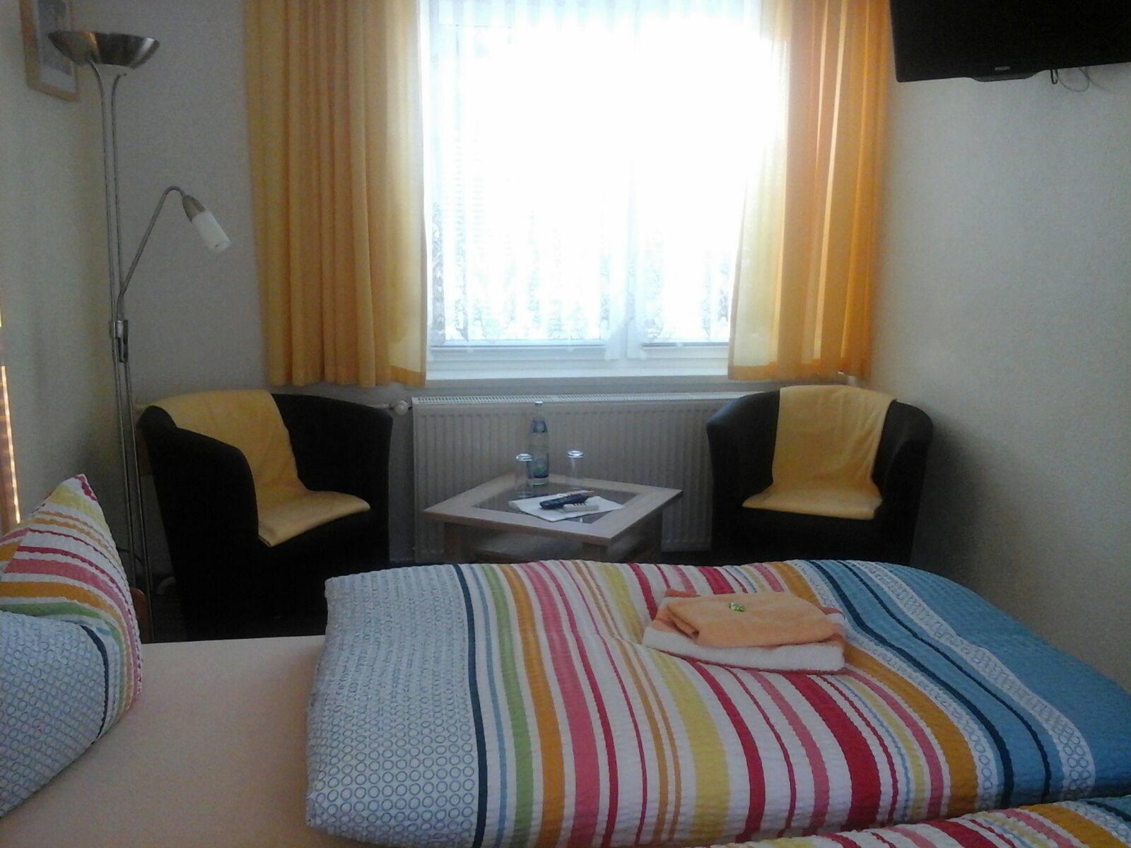 Habitación de hotel con cama, dos sillas, una mesita, ventana con cortinas y un radiador.