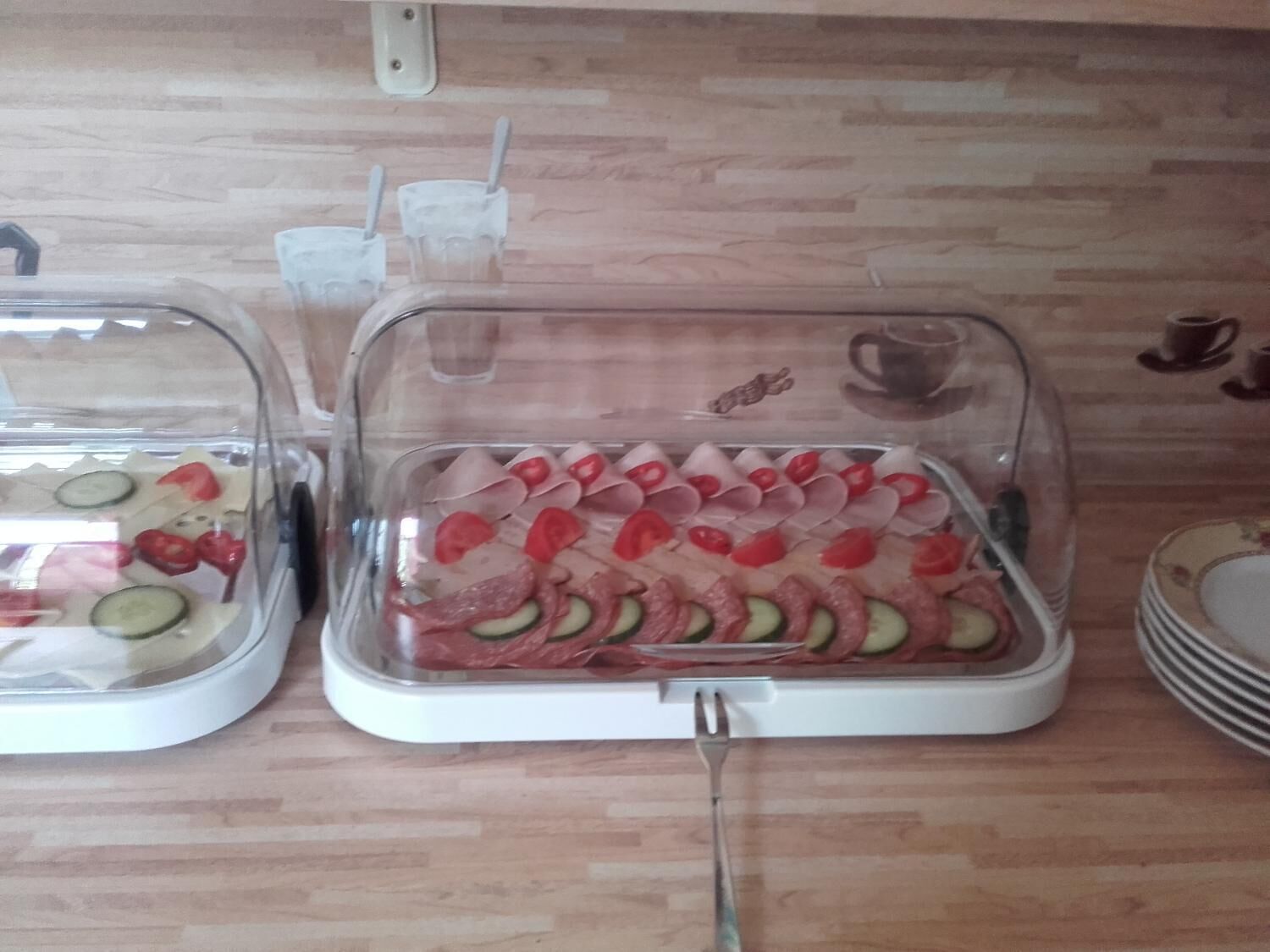Una encimera de cocina con dos dispensadores cubiertos que contienen rodajas de pepino, tomate y carne.