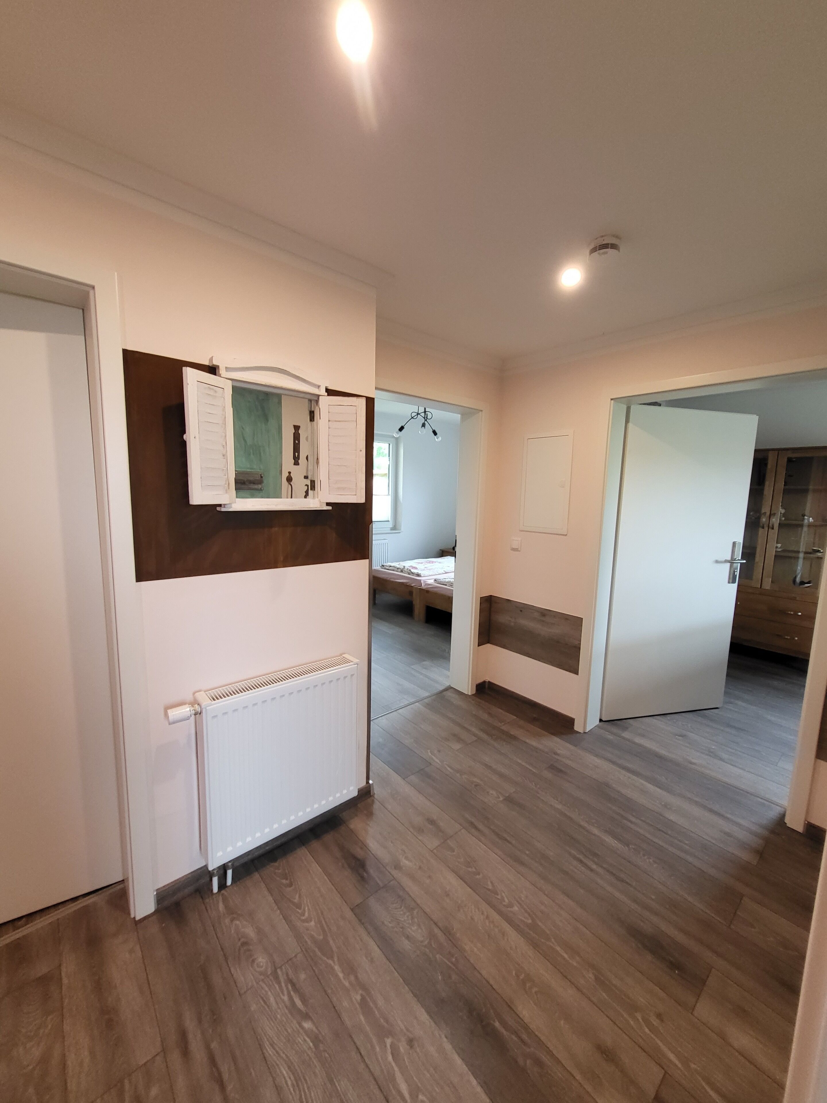 A modern, well-lit room with wooden flooring, a white radiator, and a small window with shutters.