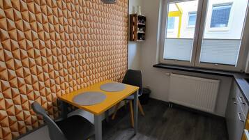 A modern kitchen with a geometric patterned wall, a dining area with a yellow table and black chairs, and a window with a view of a yellow building.