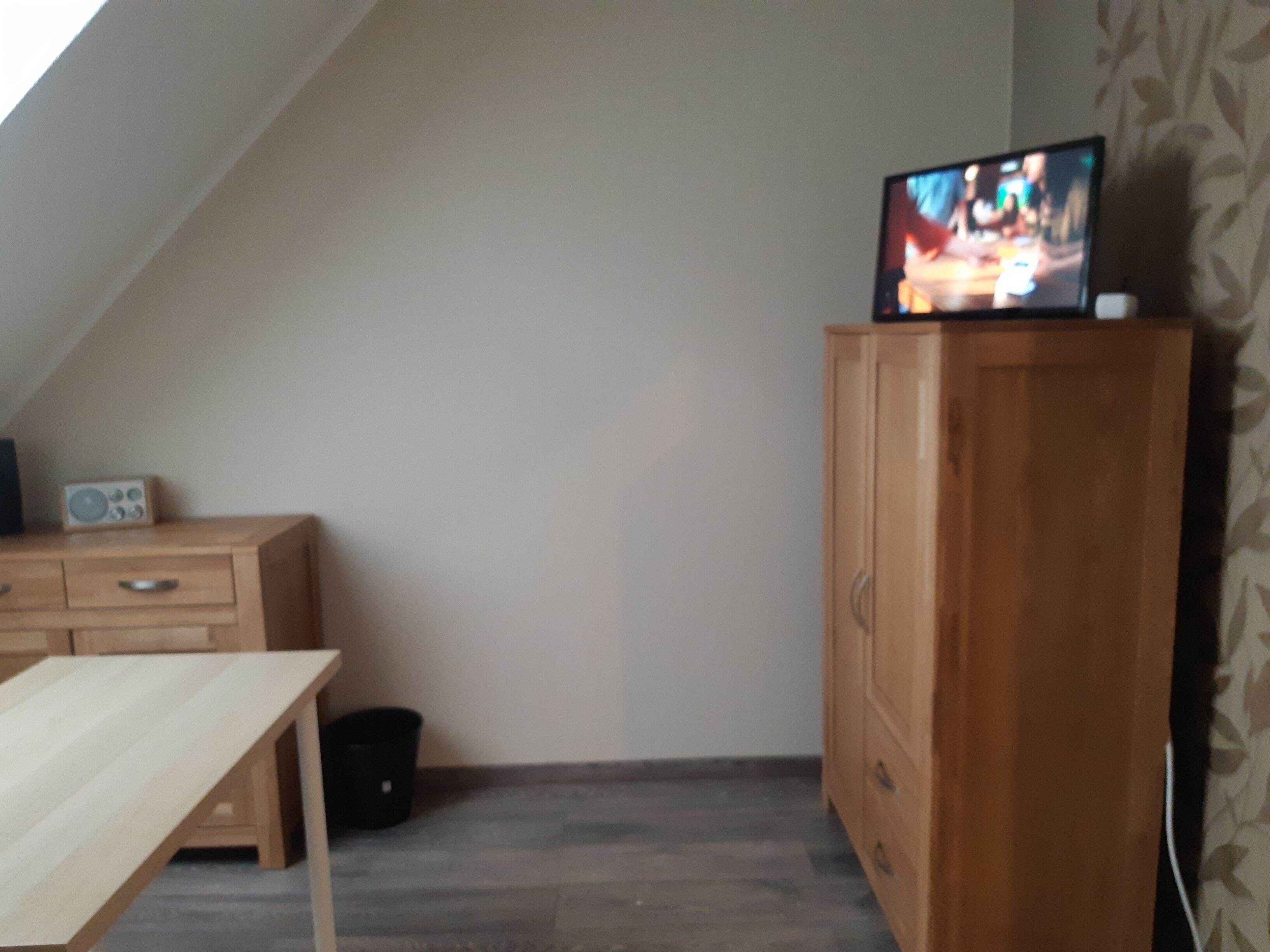 A room with a wooden cabinet, a small table, and a television on top of the cabinet.