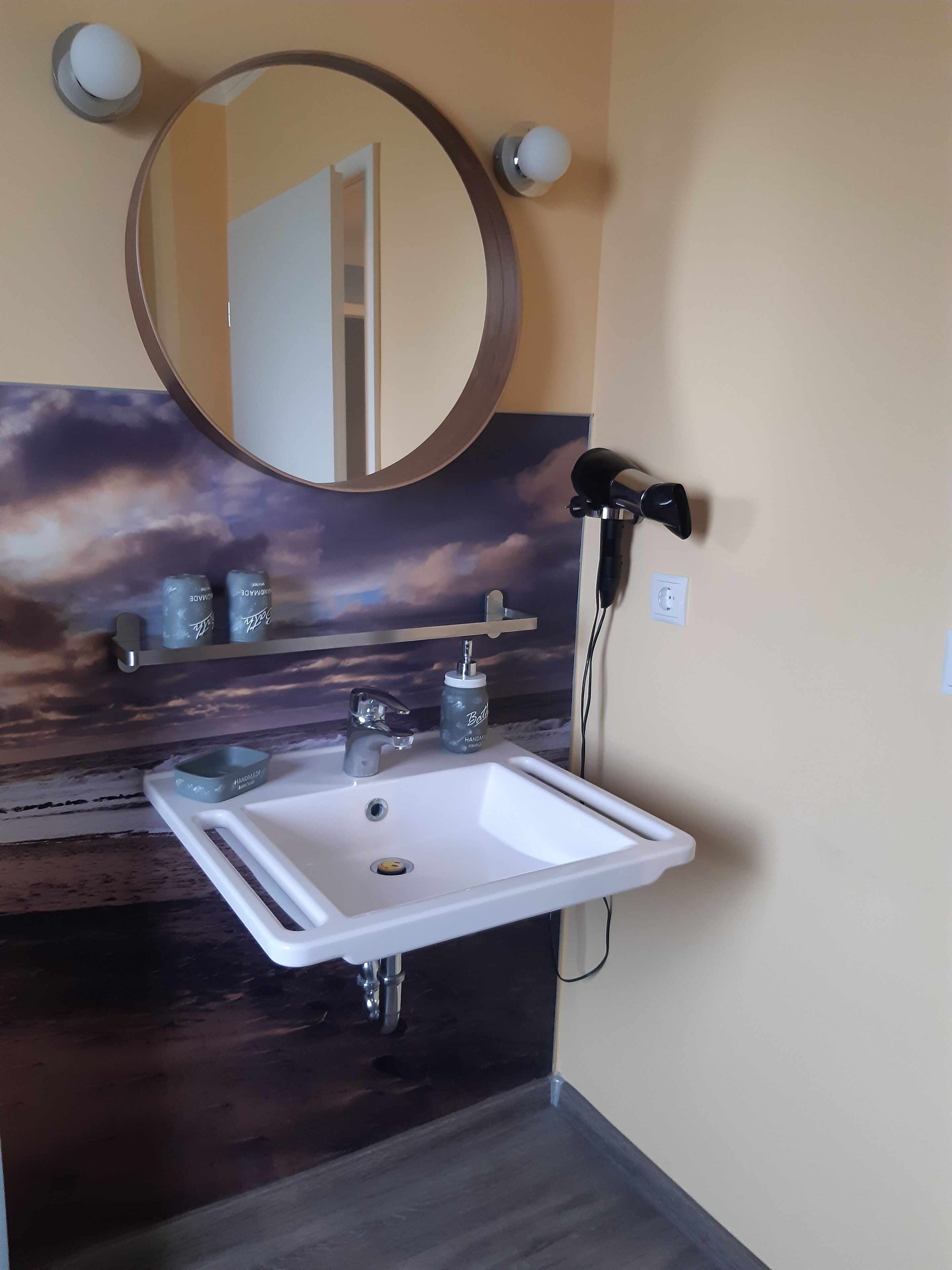 Ein Badezimmer mit einem weißen Waschbecken, einem runden Spiegel und einem Händetuchhalter an der Wand.