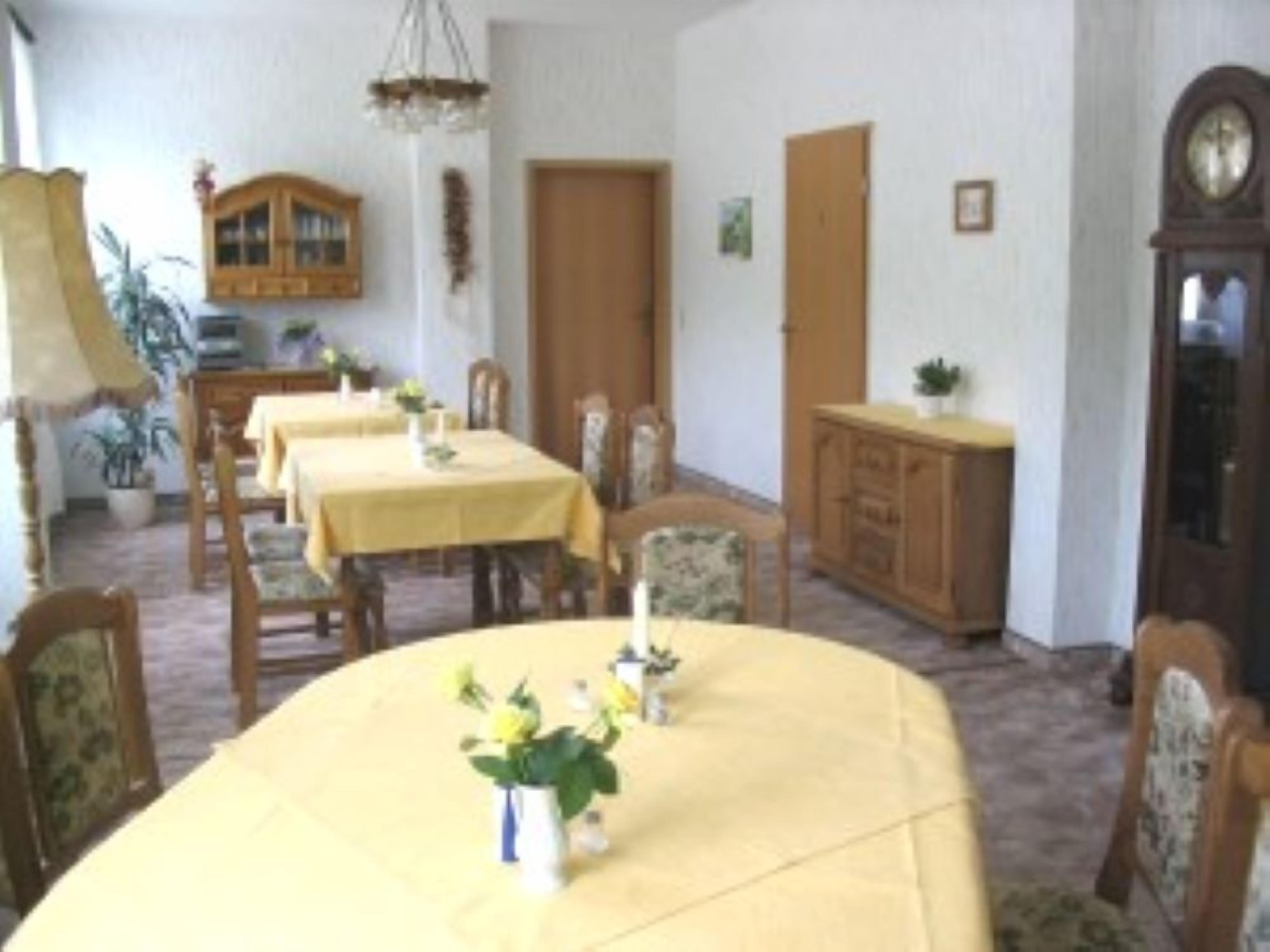 Un comedor con una gran mesa ovalada, sillas, un aparador de madera y un reloj en la pared.