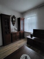Quarto com armário de madeira, relógio, televisão e janela com cortinas.