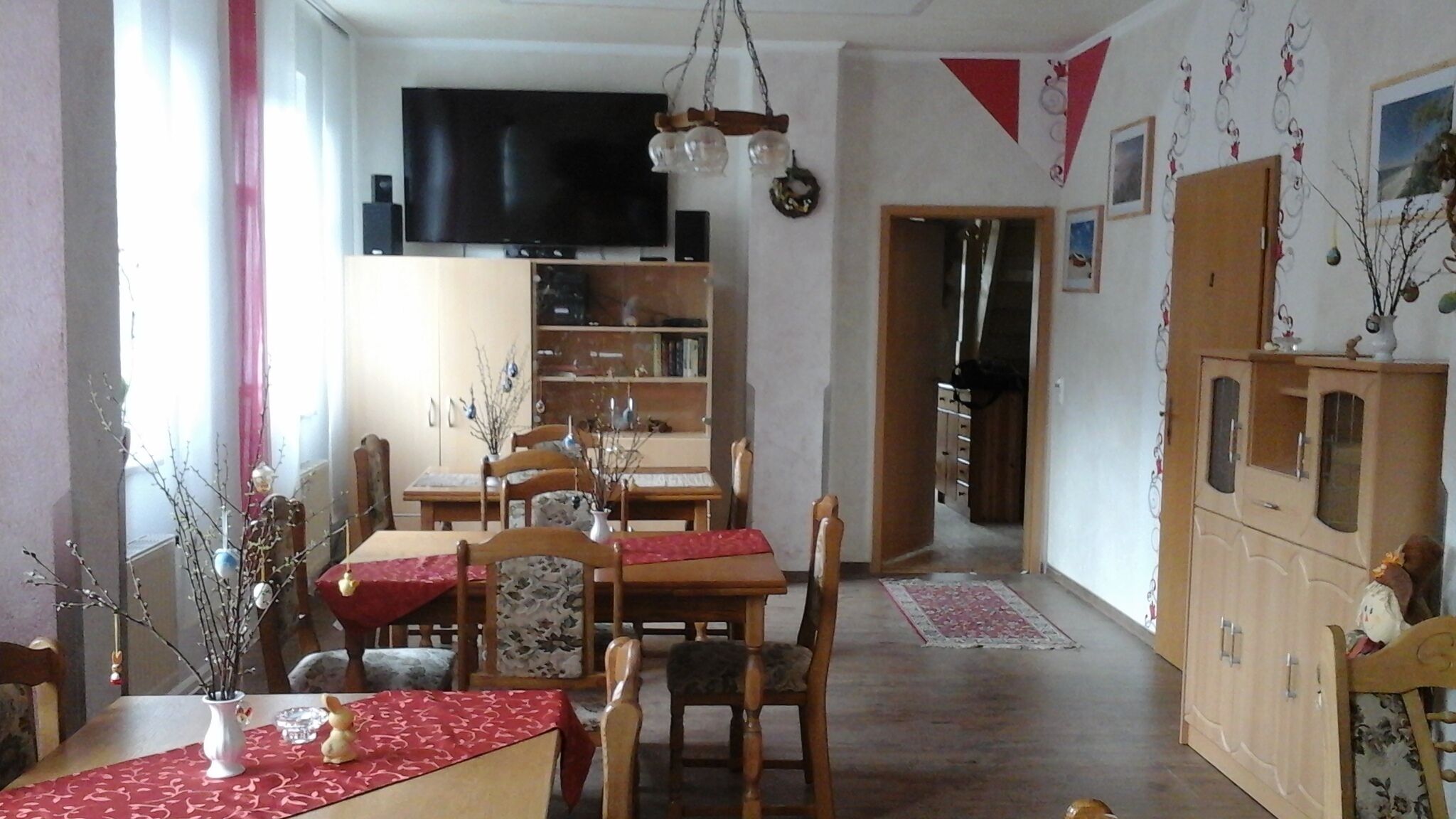 A dining area with a table set for four, a television above the table, and a bookshelf in the background.