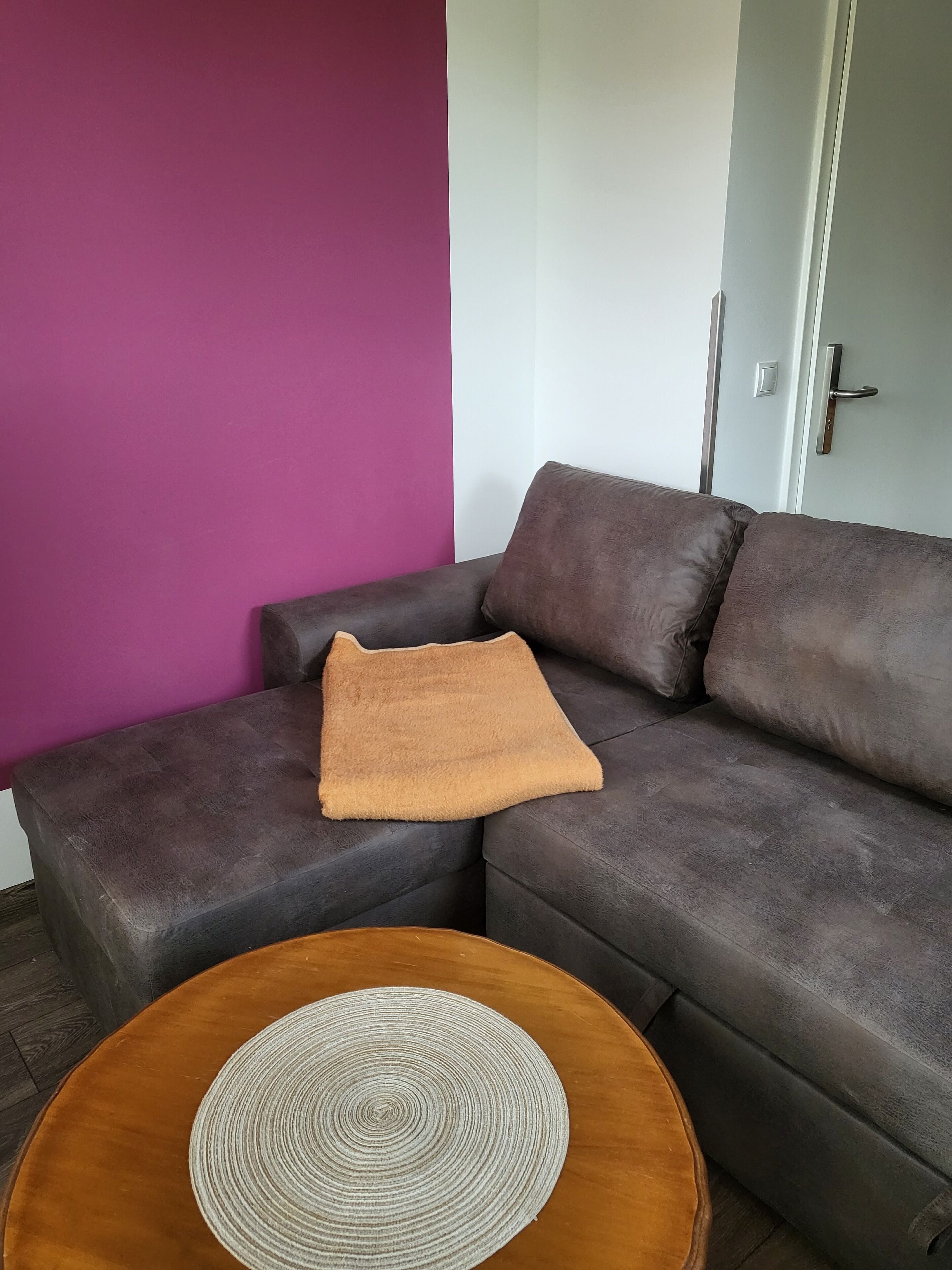 A modern living room with a dark grey sofa, a brown throw pillow, and a round wooden coffee table with a woven placemat.