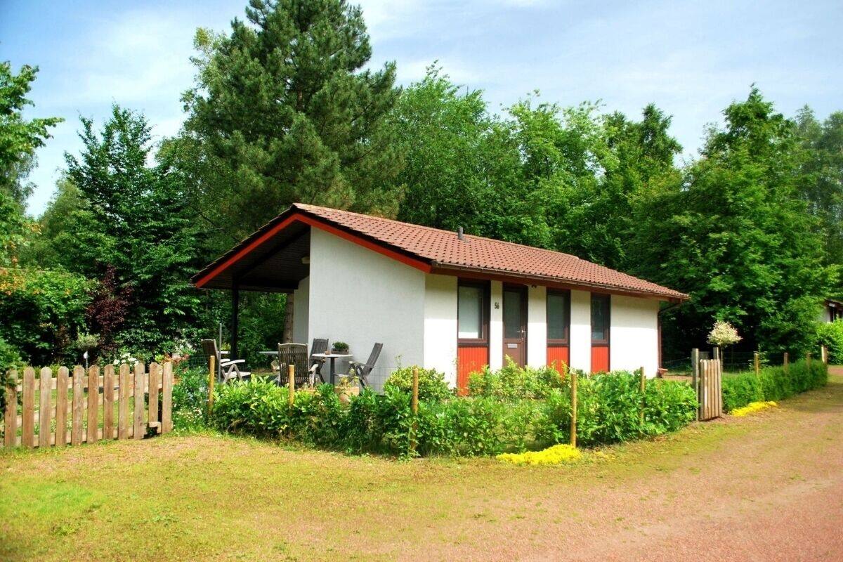 Un petit bâtiment d’un seul étage, avec un toit recouvert de tuiles rouges, entouré d’une végétation luxuriante et d’une clôture en bois.