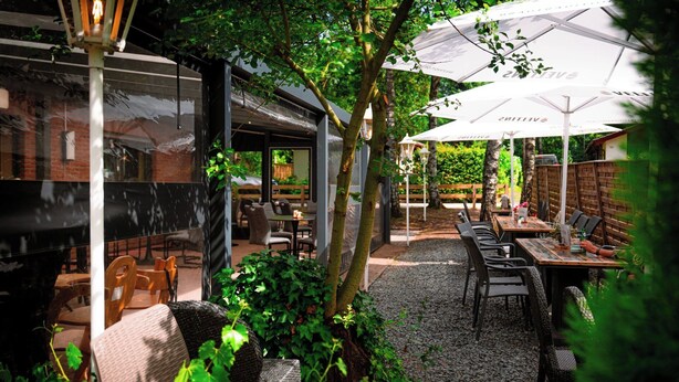 Un'area pranzo all'aperto con tavoli e sedie, immersa nel verde e alberi.