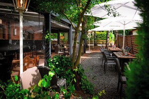 Un espace de restauration en plein air, avec des tables et des chaises, entouré de verdure et d’arbres.