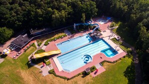 Vista aerea di un complesso piscine con scivolo, immerso nel verde e con un’area parcheggio.
