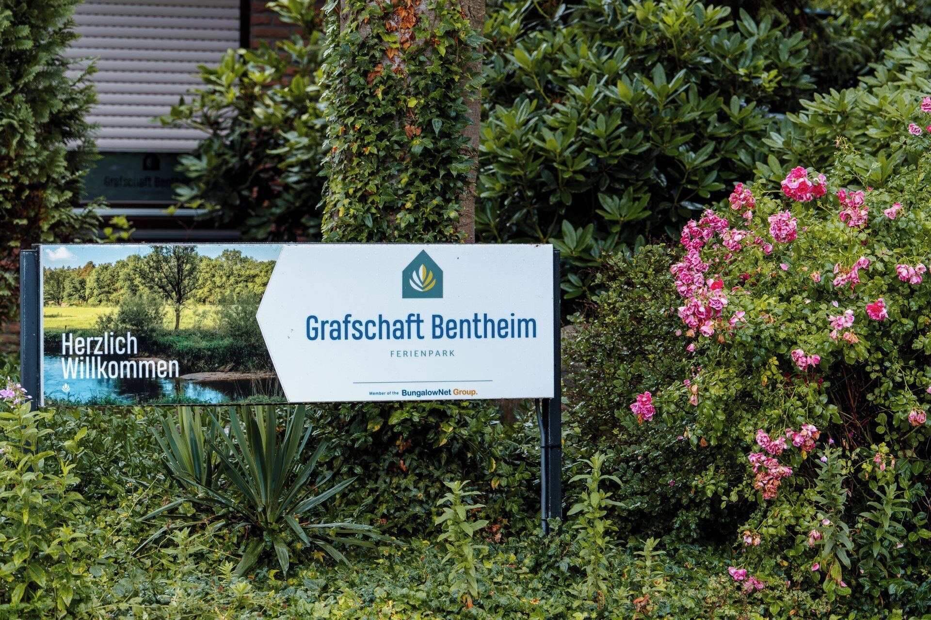 A sign for Grafshaft Bentheim, a member of the BungalowNet Group, with a scenic landscape and a river.