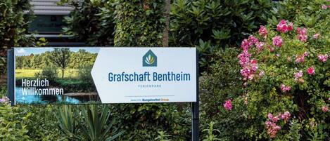 A sign for Grafshaft Bentheim, a member of the BungalowNet Group, with a scenic landscape and a river.