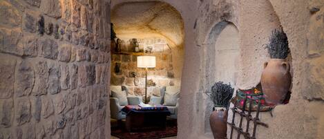 A stone-walled room with a wooden ceiling, a table with a patterned tablecloth, and a lamp.