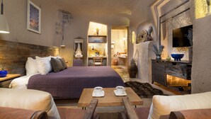 A cozy room with a bed, a wooden table with two cups, a fireplace, and a TV on the wall. - The Rupestral House Hotel (Nevsehir)