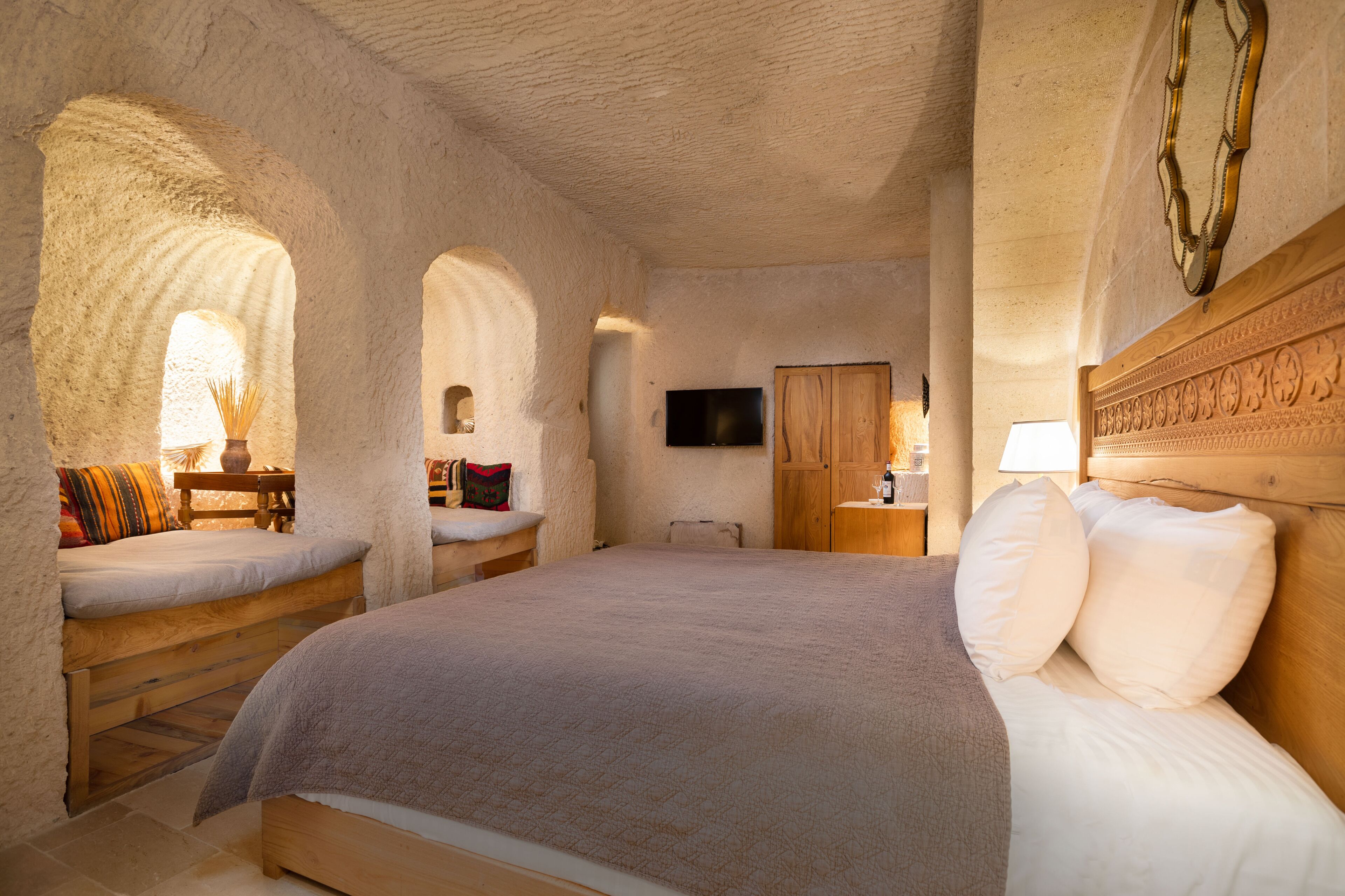 A bedroom with a large bed, wooden headboard, and a television on the wall.