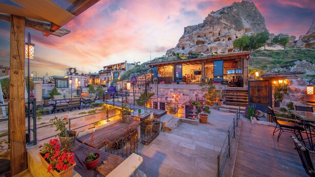 A rooftop terrace with outdoor seating, a view of a mountainous landscape, and a building with a wooden facade. - The Rupestral House Hotel (Nevsehir)