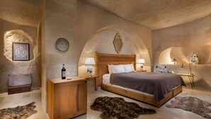 A bedroom with a wooden bed, two bedside tables with lamps, a nightstand, a decorative mirror, and a framed picture on the wall. - The Rupestral House Hotel (Nevsehir)