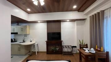 A hotel room with a bed, a TV, a small kitchenette, and a dining area.