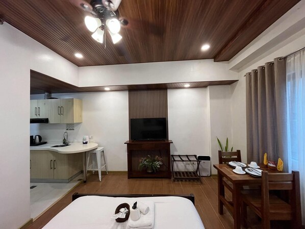 Una habitación de hotel con una cama, televisión, kitchenette y zona de comedor.