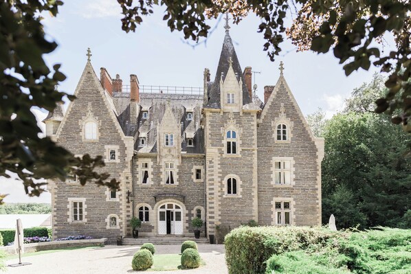 Experience the grandeur of this historic building, featuring a symmetrical facade with pointed towers and a central entrance, surrounded by beautifully manicured gardens.