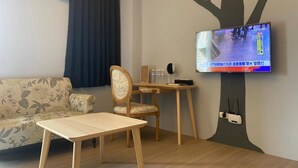 Ett vardagsrum med en soffa, ett träbord, en stol, en tv som är monterad på väggen och en väggdekor i form av ett träd.