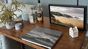 Una mesa de madera con un marco de fotografía, una botella y un pequeño objeto con forma de casa.