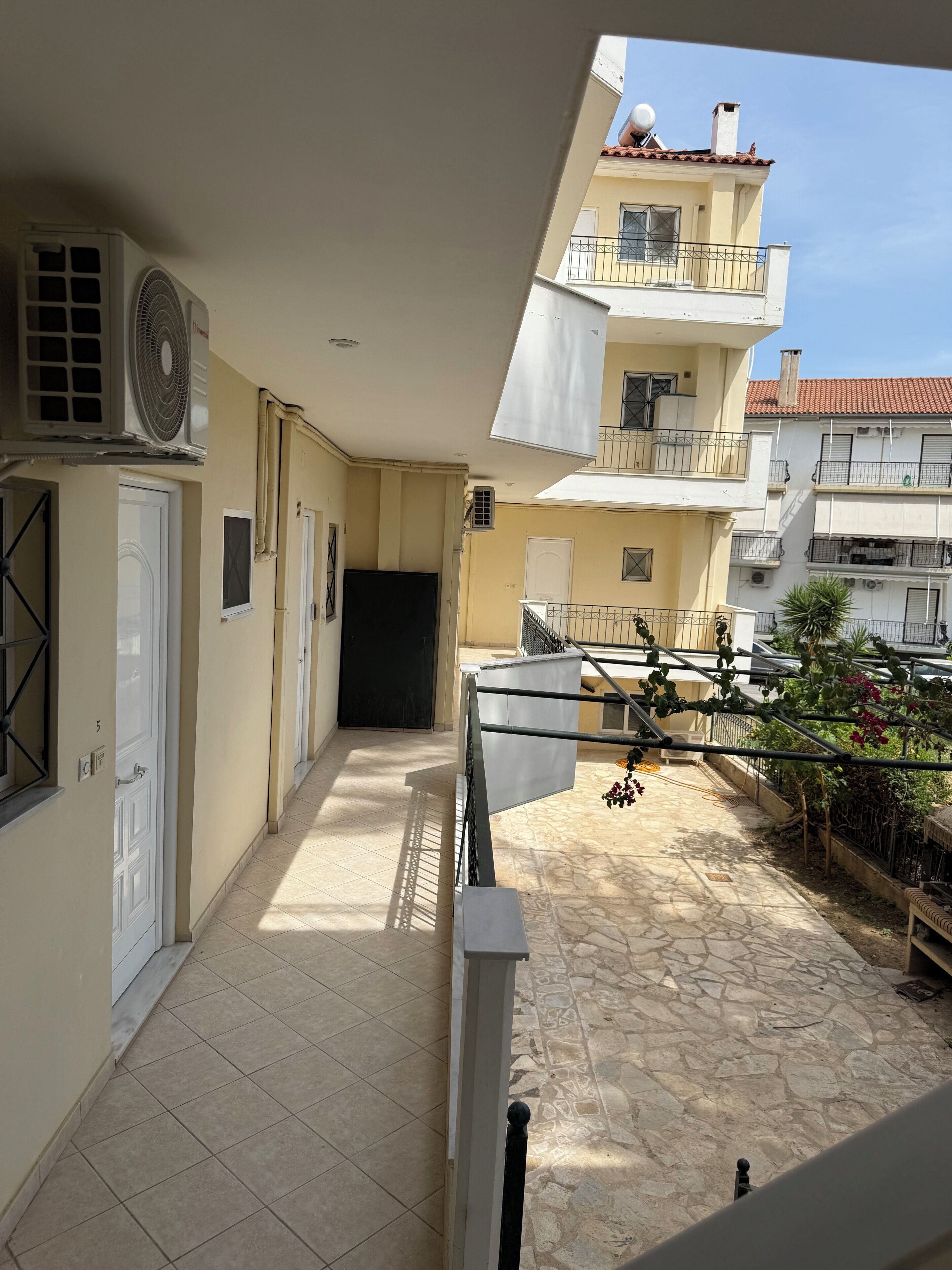 A narrow corridor with tiled flooring, a white door, and an air conditioning unit on the left.