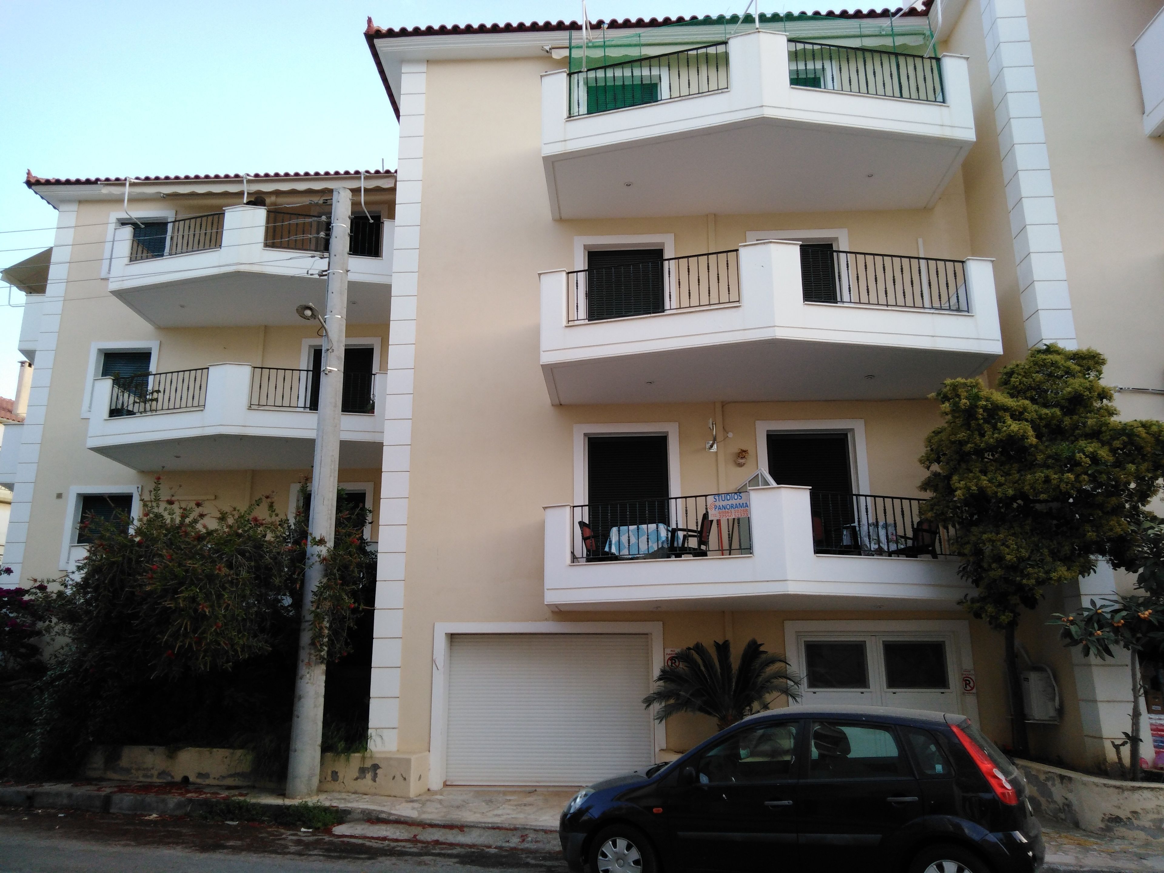 Um edifício residencial com vários andares, varandas, uma garagem e um carro estacionado.